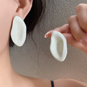 Primer plano de pendientes de esmalte blanco ovalados irregulares lucidos por modelo