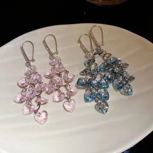 Détail macro montrant la texture des boucles d'oreilles pompons cristal coeur en rose et bleu