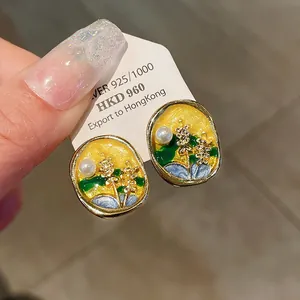 Close-up of enamel floral earrings with pearl details and a gold-tone finish.