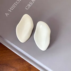 Vista detallada de pendientes ovalados color crema irregulares con acabado de esmalte brillante
