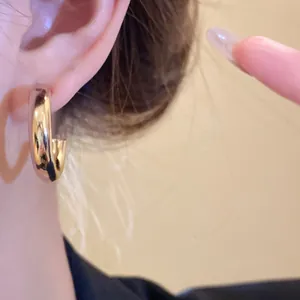 Close-up detail of smooth gold-finished geometric C-shaped hoop earrings worn on ear