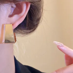 Close-up of minimalist gold-finish geometric earrings worn on ear showing shiny texture