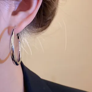Close-up detail of a minimalist polished silver geometric hoop earring worn on the ear.