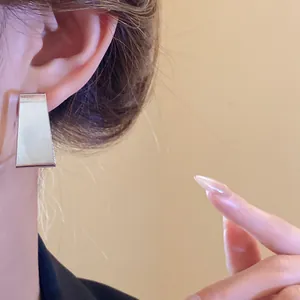 Close-up of minimalist silver geometric trapezoid stud earring worn on ear