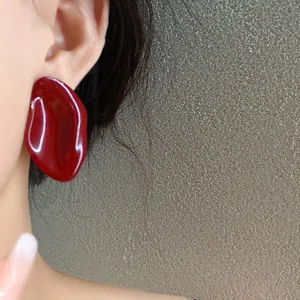 Detalle de un pendiente de botón ovalado irregular rojo vino en la oreja de una modelo