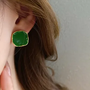 Close-up detail showing a dark green square enamel stud earring on model's ear