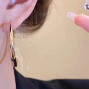 Detailed close-up shot of a thick, polished gold hoop earring worn on a model's ear.