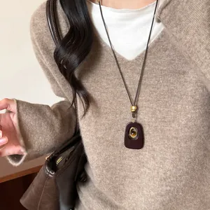 Dettaglio di una collana con pendente ovale in resina occhio di tigre su maglione beige