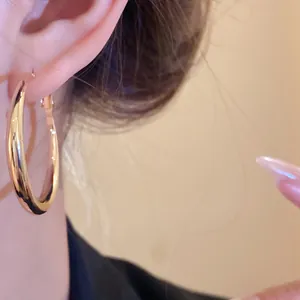 Close-up detail of a large polished gold hoop earring worn by model, minimalist style