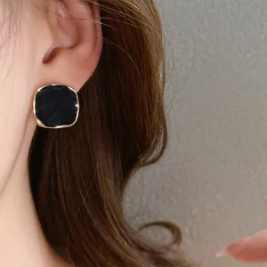 Detailed view of Korean style black oil-drip stud earring with gold border worn on ear