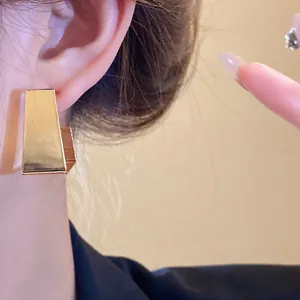 Close-up of elegant minimalist gold geometric trapezoid stud earring on woman's ear