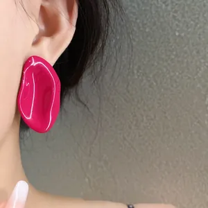 Primer plano de pendientes de esmalte magenta con forma ovalada irregular en la oreja