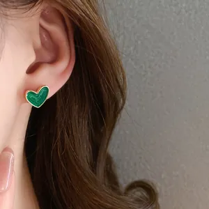 Close-up of a green enamel heart stud earring with gold-plated trim on a model's ear