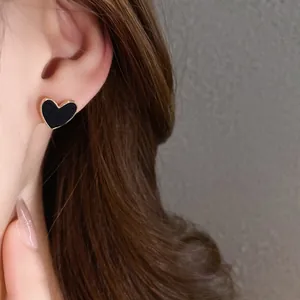 Close-up view of a minimalist black heart-shaped stud earring with a gold border