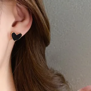 Close-up view of a minimalist black heart-shaped enamel stud earring with gold border