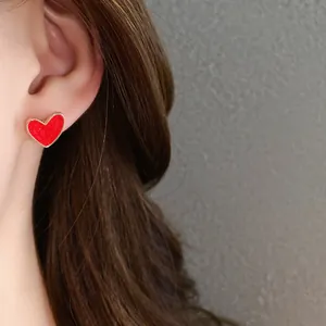 Close-up detail of a vibrant red heart-shaped stud earring with gold-tone border worn on an ear