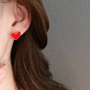 Close-up of elegant red heart-shaped stud earring with gold trim worn on ear