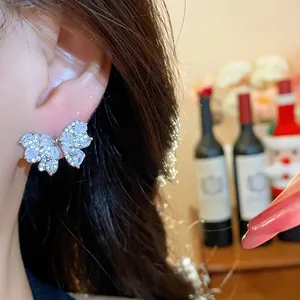 Close-up of elegant silver zircon bow stud earring on model ear, luxury aesthetic.