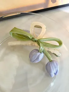 Nahaufnahme von lila Stoff-Tulpen und grünem Band an einer cremefarbenen Haarklammer aus Acryl