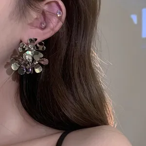 Orecchini a fiore esagerati color argento mostrati da una giovane modella asiatica
