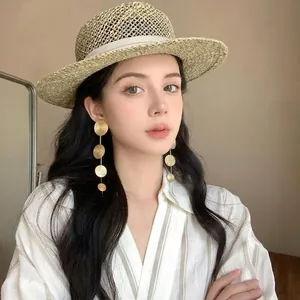 Elegant gold tiered circular disc drop earrings worn by a model with a straw hat