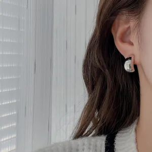 Clou d'oreille métallique argenté minimaliste en forme de C porté sur l'oreille du mannequin