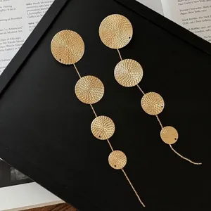 Close-up of gold tiered disc tassel earrings on a textured black background frame.