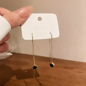 Dettaglio di eleganti orecchini a nappa dorati con pendenti quadrati neri su cartoncino