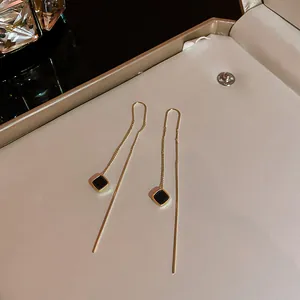 Dettaglio di eleganti orecchini a filo dorati con ciondoli geometrici quadrati neri