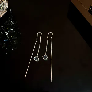 Dettaglio macro di eleganti orecchini lunghi a nappa dorati con ciondoli neri quadrati