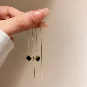 Primo piano di lunghi orecchini a catenella dorati con pendenti neri