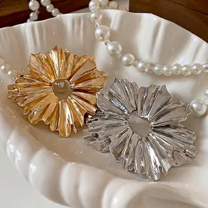 Elegant gold and silver pleated metal flower earrings displayed in a shell dish