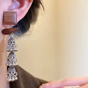 Detailansicht von ethnischen Holzohrringen mit silbernen Glockenquasten beim Tragen.