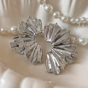 Close-up detail of silver metallic flower fan-shaped pleated earrings on a pearl background.