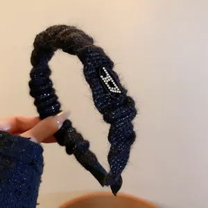 Elegant black knitted headband with rhinestone 'D' logo, padded for high top volume.