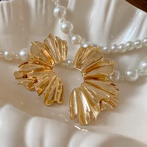 Close-up detail of gold-tone pleated fan-shaped metal earrings with artistic texture