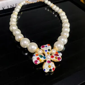 Detailed view of pearl necklace with a colorful rhinestone flower pendant on black background