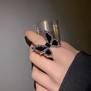 Close-up detail of a large black butterfly ring with pleated silver borders worn on a hand