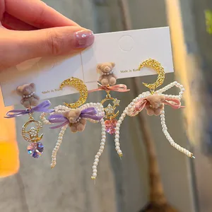 Close-up detail of sweet teddy bear earrings with pearls, bows and moon charms