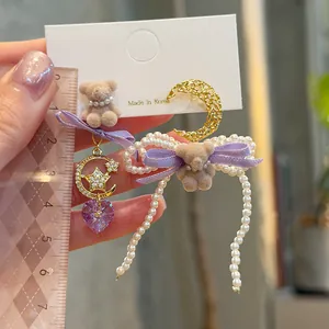 Close-up view of cute bear and pearl bow earrings featuring a purple heart crystal