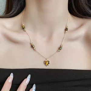 Detailed view of vintage tiger eye beaded necklace with golden heart pendant on model.