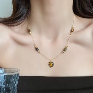Detailed view of elegant gold necklace with tiger eye beads and heart pendant on model
