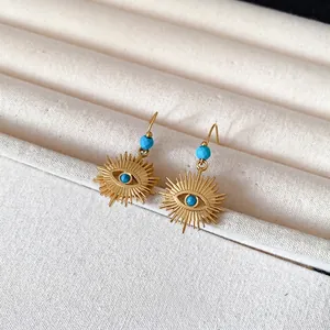 Vintage gold sunburst evil eye dangle earrings with blue beads on beige display
