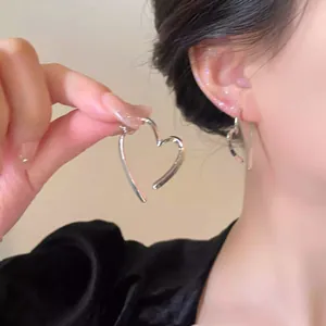 Nahaufnahme von minimalistischen herzförmigen Creolen in Silber am Ohr einer Frau getragen
