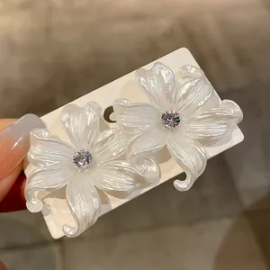 Primer plano de elegantes pendientes de flores blancas con circón brillante en tarjeta.