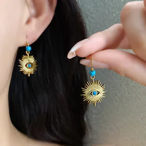 Detail shot of vintage golden sun eye dangle earrings with turquoise beads worn by a model