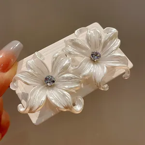 Primer plano de pendientes de flores blancas con circón central en tarjeta blanca