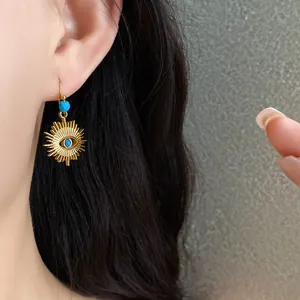 Close-up view of gold sunburst evil eye drop earring featuring blue turquoise accent beads