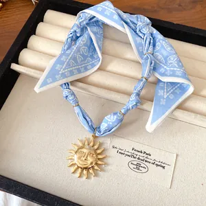 Close-up of a vintage sun face pendant on a blue paisley fabric strap