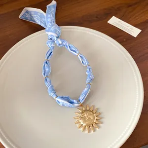 Macro view of blue patterned fabric necklace with vintage gold sun face pendant